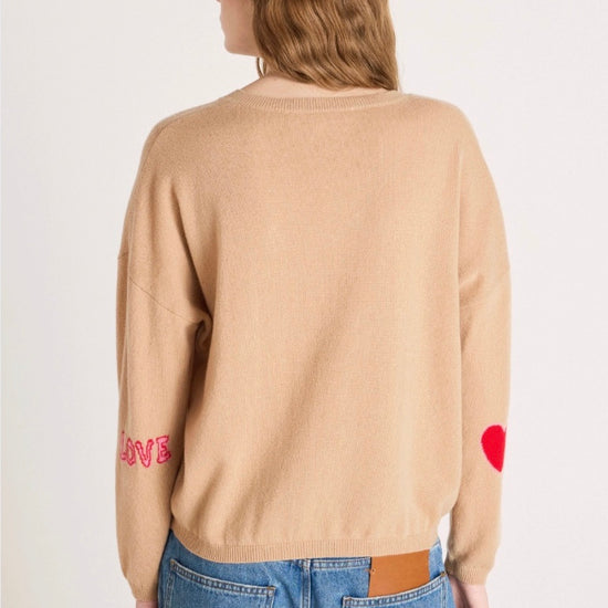Woman wearing a beige sweater with text and blue jeans on a white background