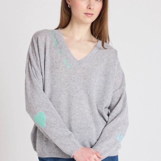 Woman wearing a gray sweater with heart patterns on a plain background