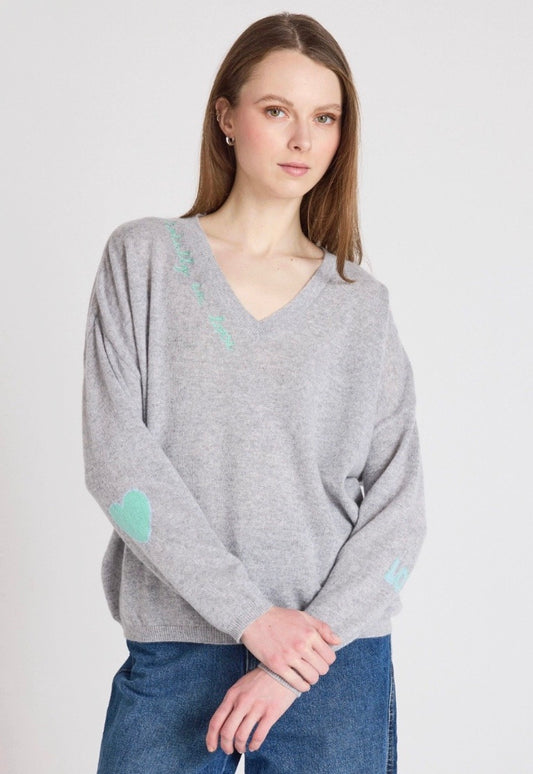 Woman wearing a gray sweater with heart patterns on a plain background