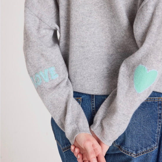 Woman wearing a gray sweater with heart patterns on a plain background