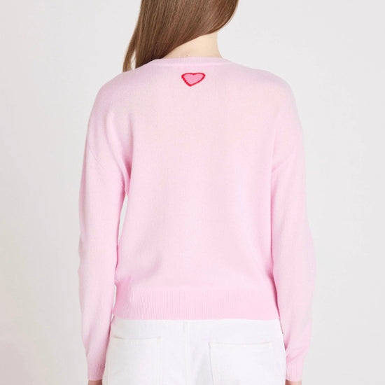 Person wearing a pink sweater with a heart design on the back, standing against a plain background.