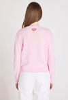 Person wearing a pink sweater with a heart design on the back, standing against a plain background.