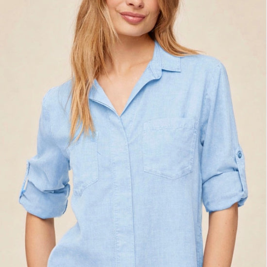 Woman wearing a light blue shirt with rolled-up sleeves against a beige background