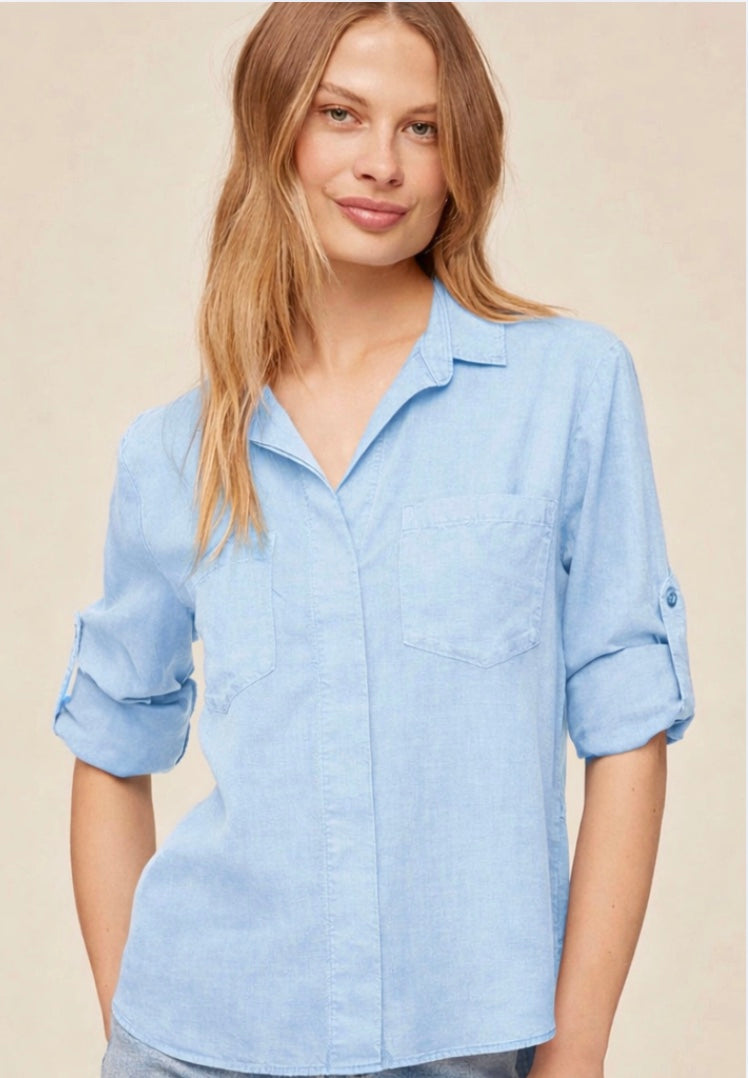 Woman wearing a light blue shirt with rolled-up sleeves against a beige background