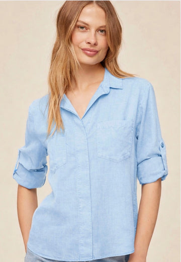 Woman wearing a light blue shirt with rolled-up sleeves against a beige background