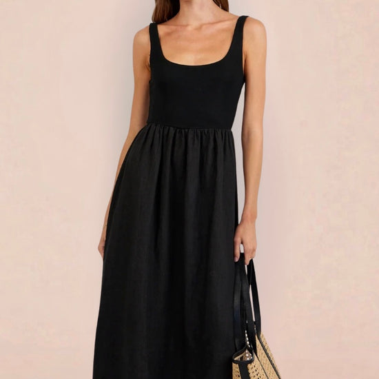 Woman wearing a black sleeveless dress holding a woven bag on a beige background