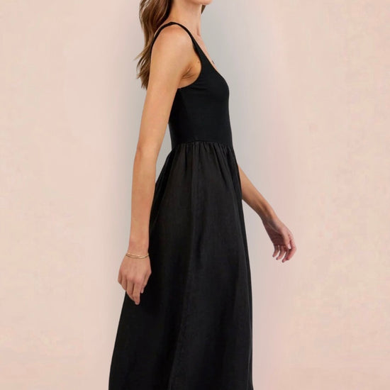 Woman wearing a black sleeveless dress holding a woven bag on a beige background