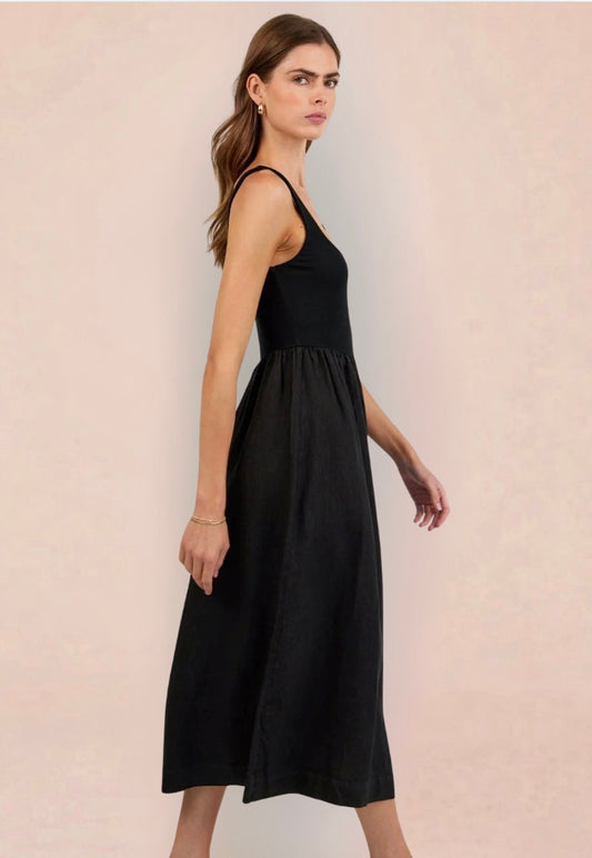 Woman wearing a black sleeveless dress holding a woven bag on a beige background