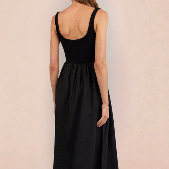 Woman wearing a black sleeveless dress holding a woven bag on a beige background