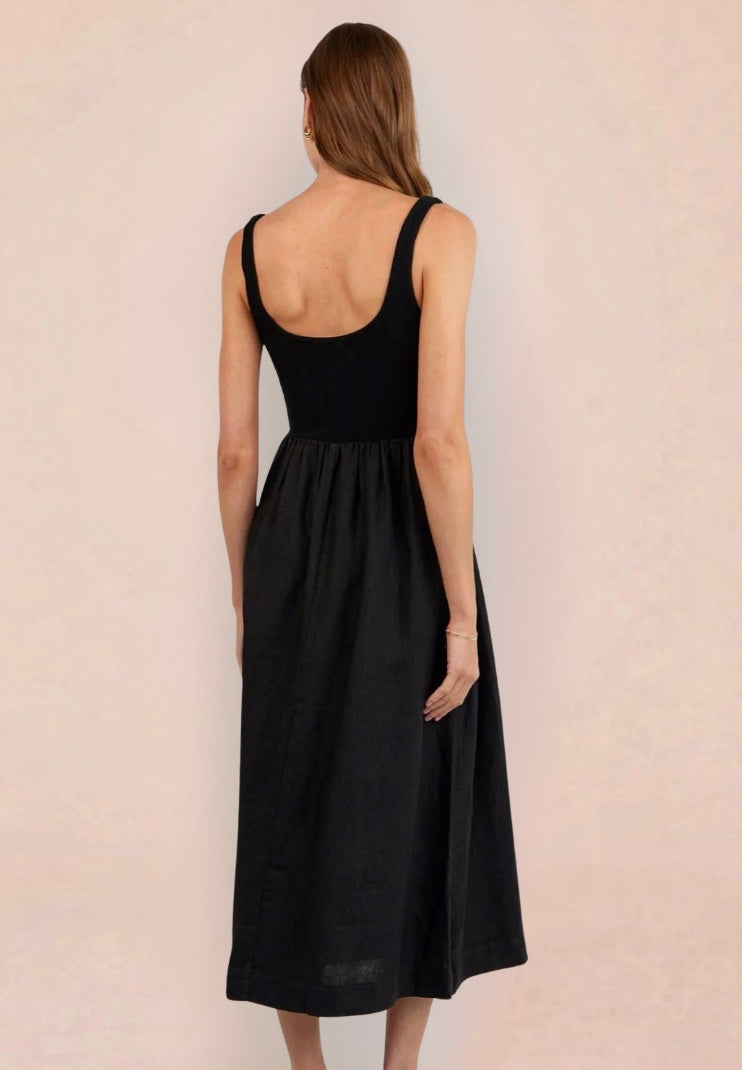 Woman wearing a black sleeveless dress holding a woven bag on a beige background