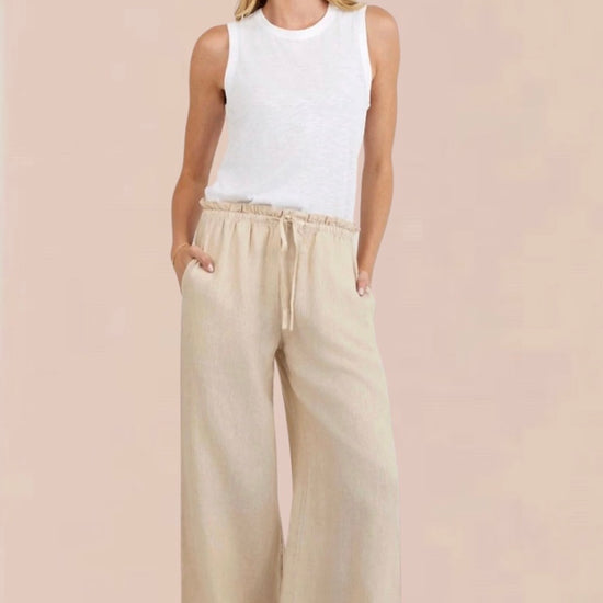 Woman wearing a white sleeveless top and beige wide-leg pants 