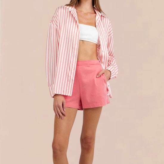 Woman wearing a pink and white striped shirt and shorts on a beige background