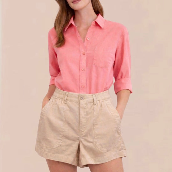 Woman wearing a pink shirt and beige shorts on a plain background