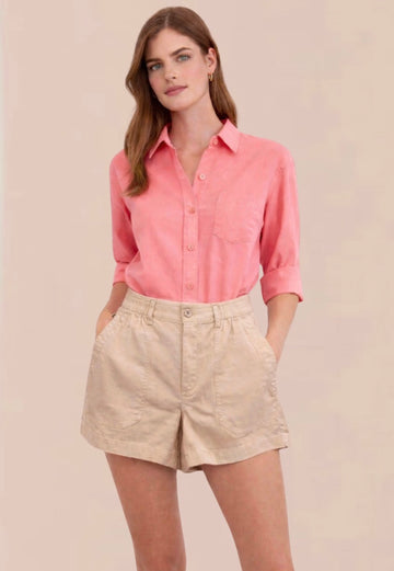 Woman wearing a pink shirt and beige shorts on a plain background