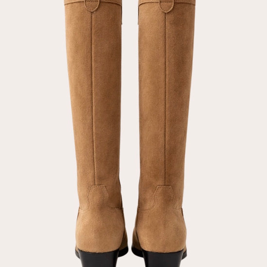 Tan knee-high  cow boy boot with a black block heel on a light beige background