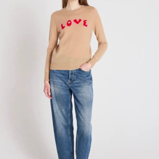 Woman wearing a beige sweater with 'LOVE' print and blue jeans on a white background