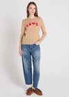 Woman wearing a beige sweater with 'LOVE' print and blue jeans on a white background