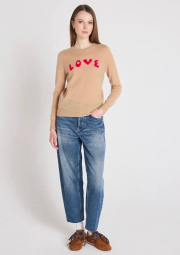 Woman wearing a beige sweater with 'LOVE' print and blue jeans on a white background