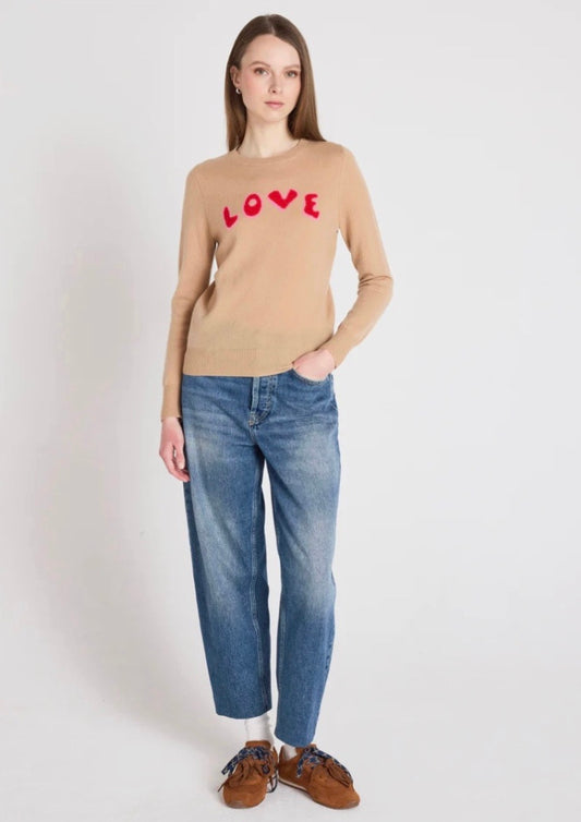 Woman wearing a beige sweater with 'LOVE' print and blue jeans on a white background
