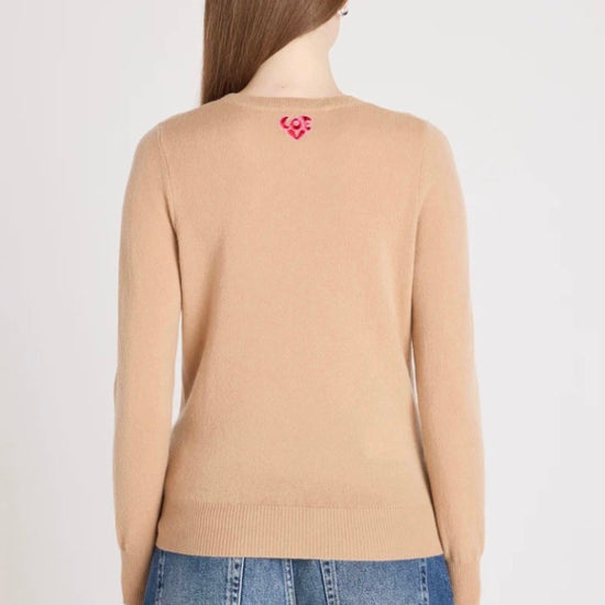 Person wearing a beige sweater with a red heart design on the back, standing against a plain background.