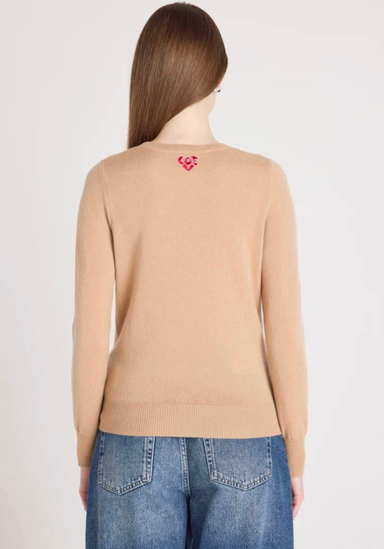 Person wearing a beige sweater with a red heart design on the back, standing against a plain background.