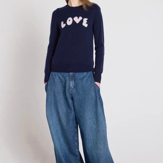 Person wearing a navy sweater with 'LOVE' text and wide-leg jeans on a white background