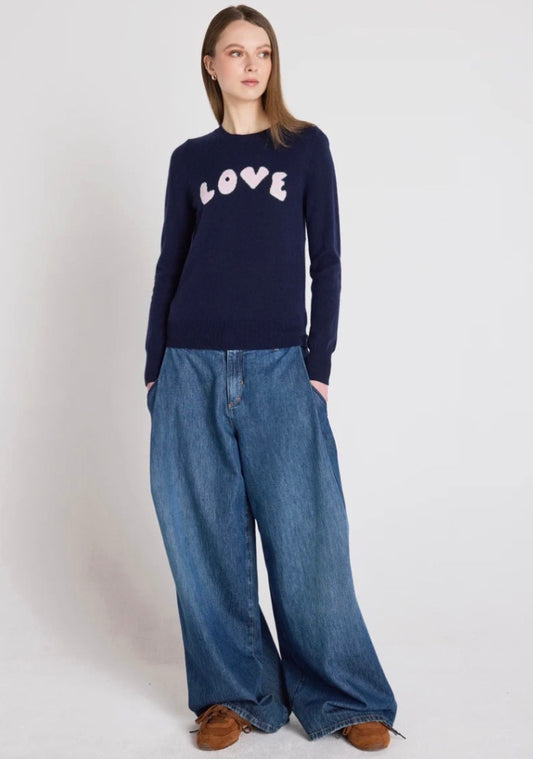 Person wearing a navy sweater with 'LOVE' text and wide-leg jeans on a white background