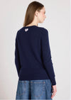 Woman wearing a navy sweater with a heart design on the back, standing against a light gray background.