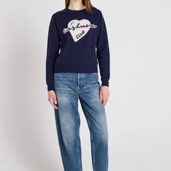 Model wearing a navy jumper and blue jeans on a white backgrounds