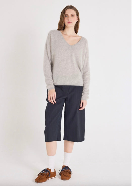 Woman wearing a gray sweater and navy pants on a white background