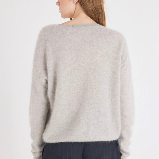 Person wearing a light gray sweater and dark pants on a white background
