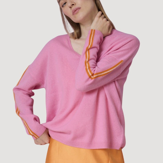 Person wearing a pink sweater with orange accents on a plain background