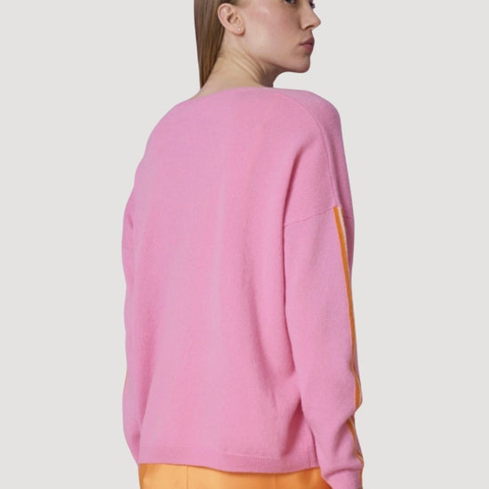Person wearing a pink sweater and orange pants on a light gray background