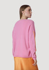 Person wearing a pink sweater and orange pants on a light gray background