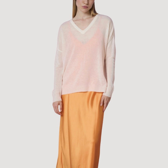 Woman wearing a light pink sweater and mustard yellow skirt on a white background