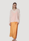 Woman wearing a light pink sweater and mustard yellow skirt on a white background