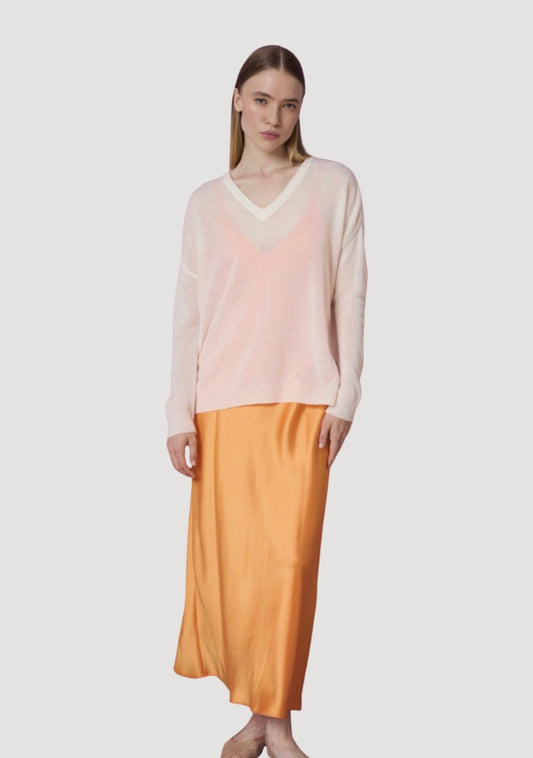 Woman wearing a light pink sweater and mustard yellow skirt on a white background