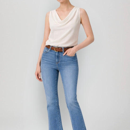 Woman wearing a white sleeveless top and blue jeans on a plain background
