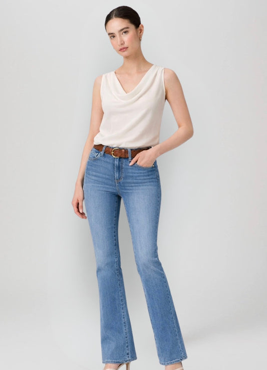 Woman wearing a white sleeveless top and blue jeans on a plain background