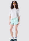 Woman wearing a white oversized shirt and light green shorts on a white background