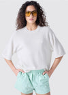 Person wearing a white oversized t-shirt and light green striped shorts on a plain background