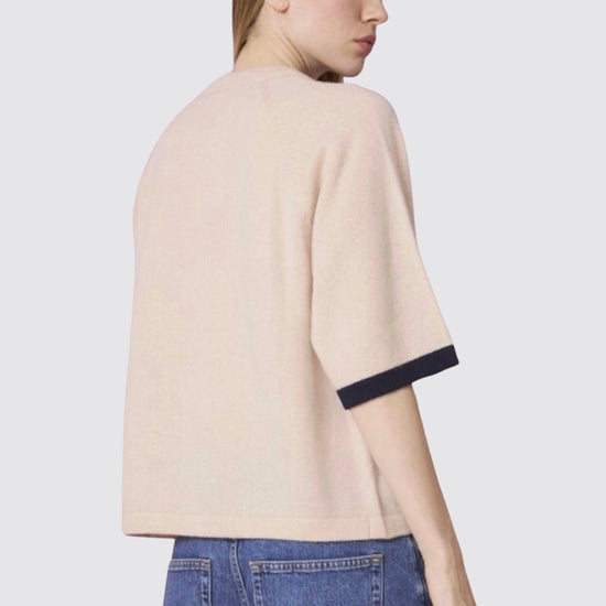 Person wearing a beige sweater with black trim and blue jeans on a light gray background