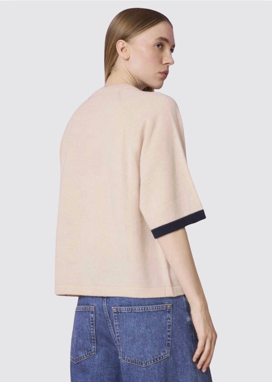 Person wearing a beige sweater with black trim and blue jeans on a light gray background