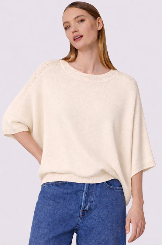 Woman wearing a beige oversized sweater and blue jeans on a light gray background