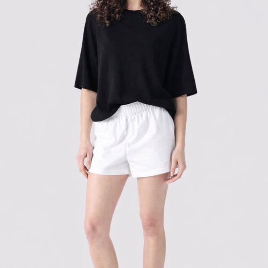 Person wearing a black oversized shirt, white shorts, and sunglasses on a light gray background