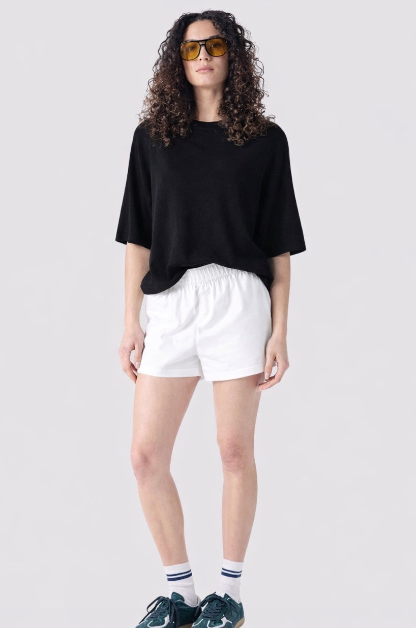 Person wearing a black oversized shirt, white shorts, and sunglasses on a light gray background