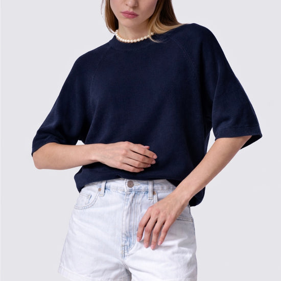 Woman wearing a navy sweater and white shorts on a plain background