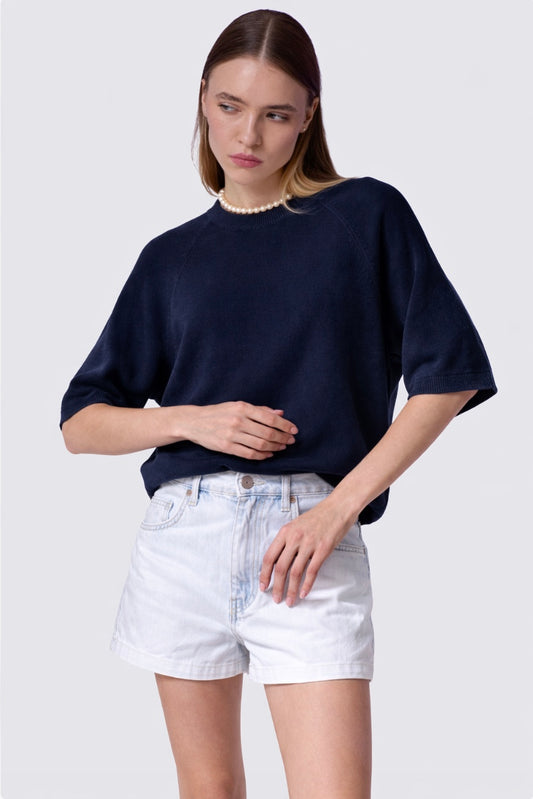 Woman wearing a navy sweater and white shorts on a plain background