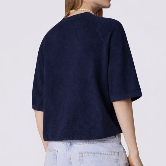 Person wearing a navy blue cashmere knit and light blue jeans on a white background