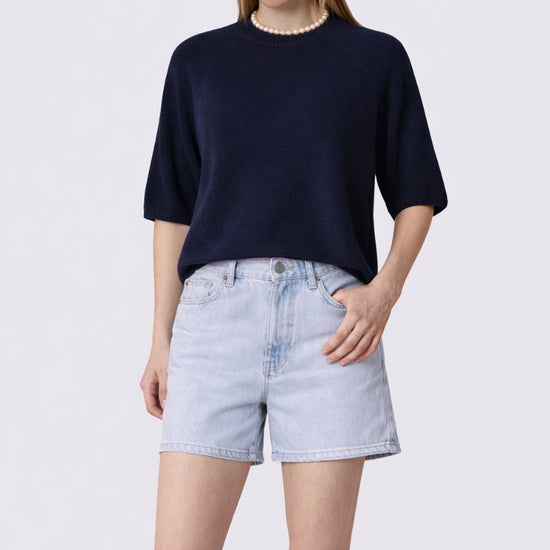 Woman wearing a navy blue top and light denim shorts on a white background